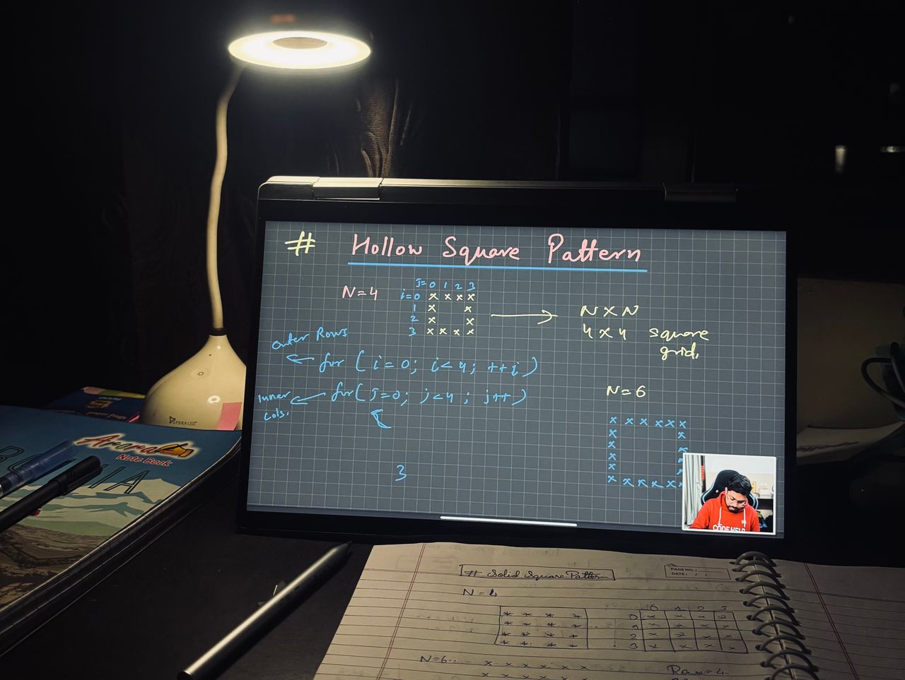 A dimly lit home study setup with laptop displaying coding notes on a hollow square pattern.